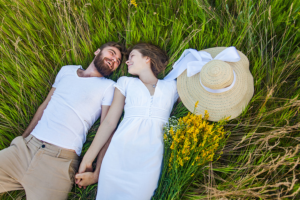 Happy young relaxed couple in love laying down on the grass overhead