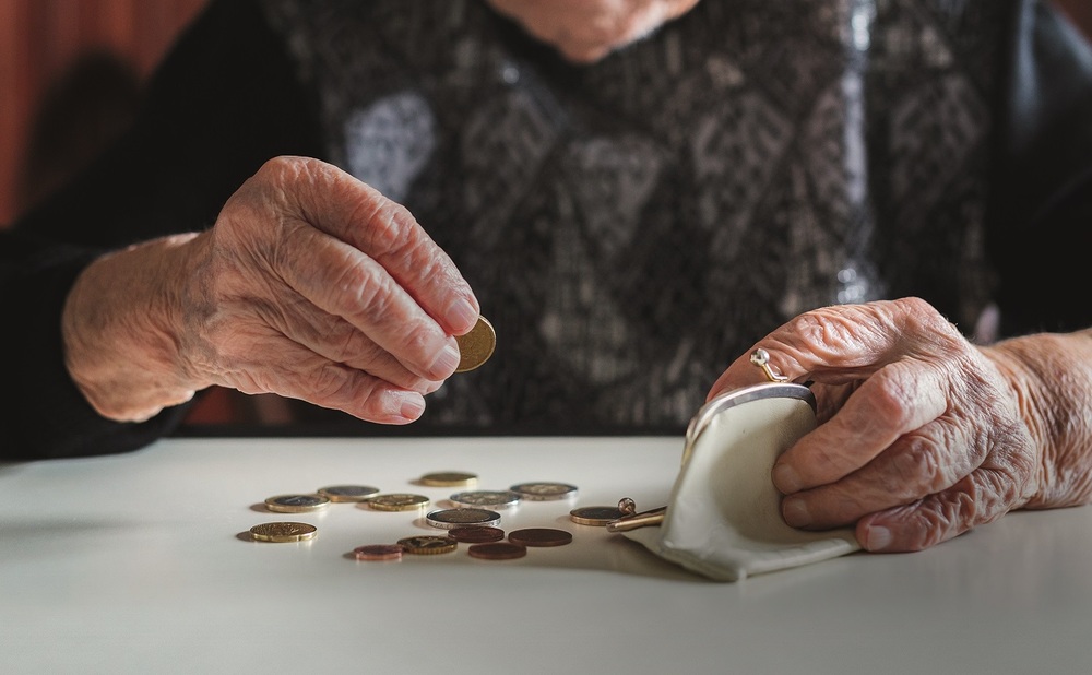 Elderly 95 years old woman sitting miserably at the table at home and counting remaining coins from the pension in her wallet after paying the bills.